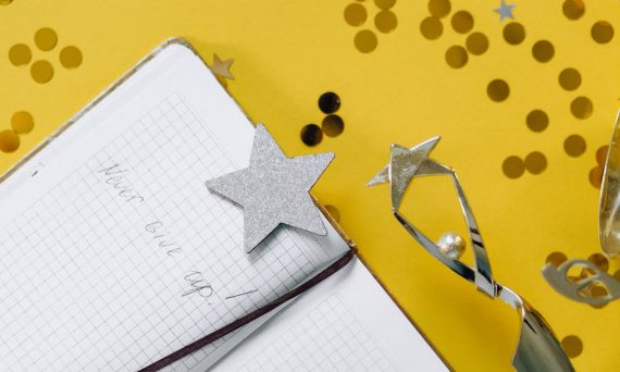 Flat lay of a notebook with motivational text, trophy, and star confetti on a yellow background.